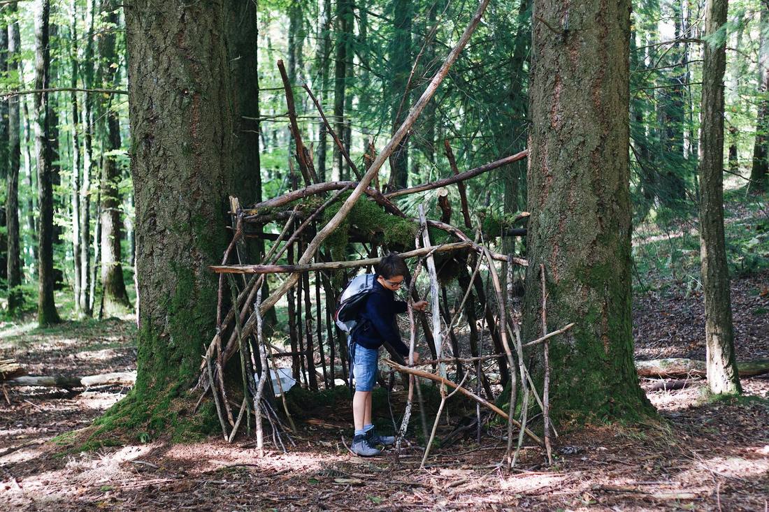 Un enfant assemblant des branches pour construire un abri dans une forêt