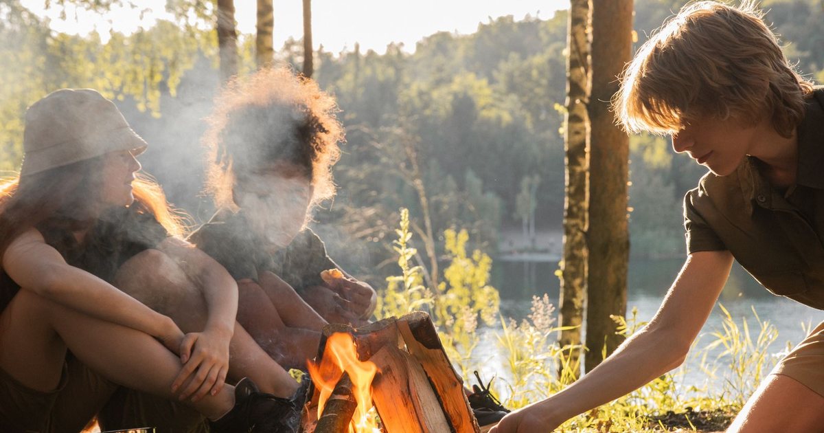 Enfants et adolescent autour d'un feu de camp en forêt au bord d'un lac, lors d'une journée nature