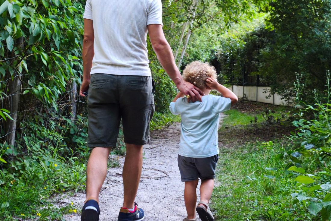 Un adulte et un enfant marchant main dans la main sur un sentier forestier