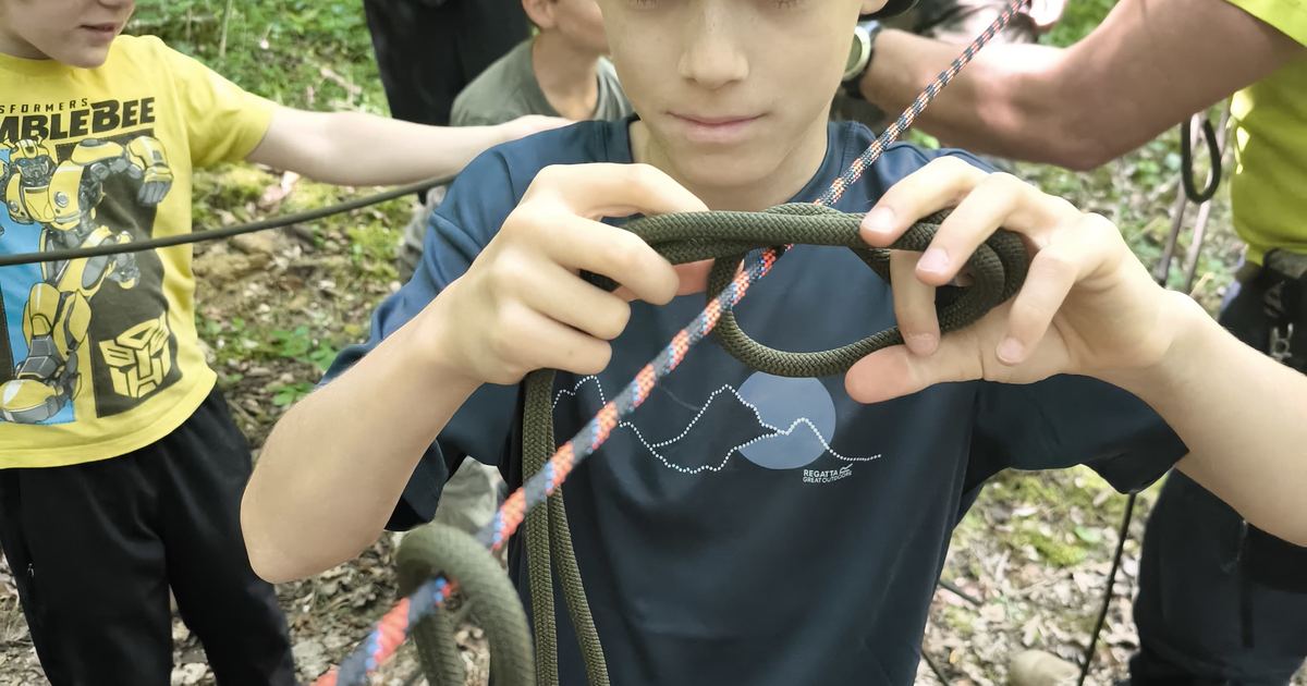 Enfant apprenant un nœud avec un adulte lors d'un stage nature en famille