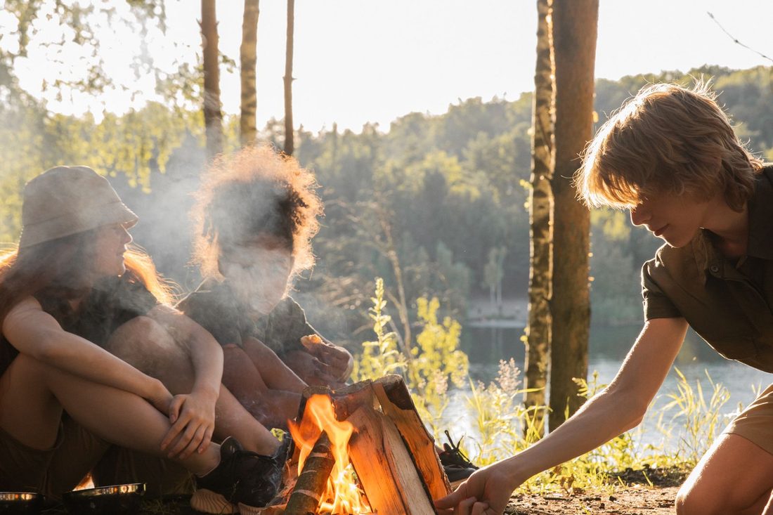 Jeunes réunis autour d'un feu de camp en forêt à la tombée du jour